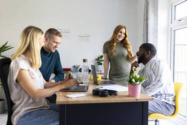 Smiling business colleagues talking at desk in office - WPEF06599