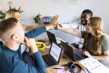 Smiling multiracial business colleagues giving high-five at workplace - WPEF06658