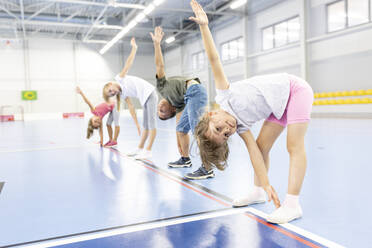 Elementary students doing stretching exercise with each other at school sports court - WESTF25127