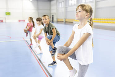 Girl stretching leg with students at school sports court - WESTF25129