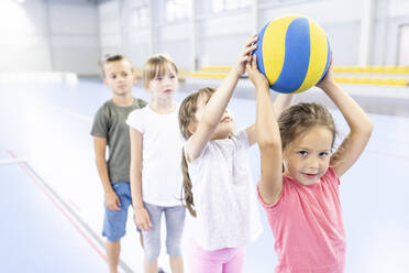 Girl passing ball to friend standing in line at school sports court - WESTF25130