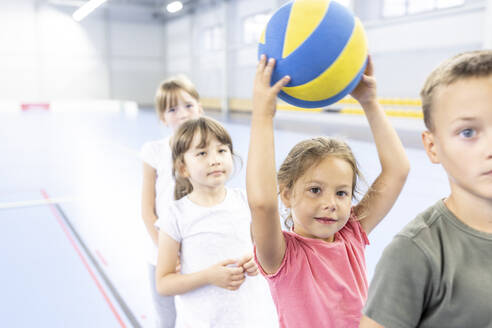 Grundschülerin, die einen Ball hält und mit ihren Freunden auf dem Sportplatz in einer Reihe steht - WESTF25132