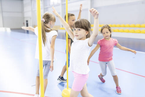 Grundschüler mit erhobenen Armen, die auf dem Schulsportplatz um eine Stange laufen - WESTF25135