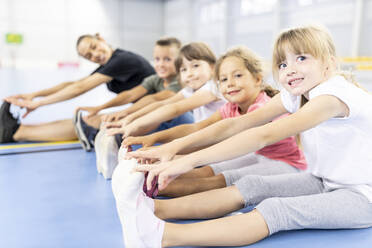 Lächelnde Grundschüler, die Seite an Seite mit ihrem Lehrer auf dem Schulsportplatz sitzen - WESTF25141