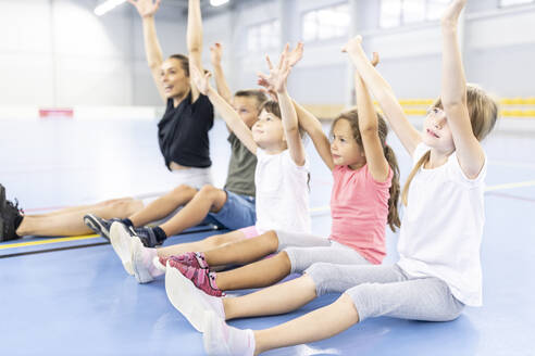 Schüler bei einer Übung im Sitzen mit erhobenen Armen durch einen Lehrer auf dem Schulsportplatz - WESTF25143