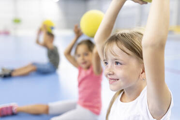 Smiling girl with arms raised by friends at school sports court - WESTF25146