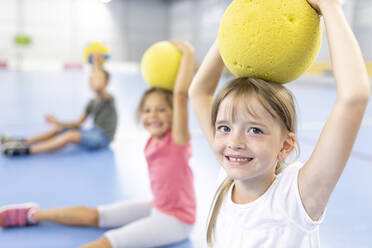 Lächelndes Mädchen hält Ball auf dem Kopf auf dem Schulsportplatz - WESTF25147