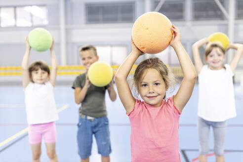 Lächelndes Mädchen hält Ball auf dem Schulsportplatz mit Freunden im Hintergrund - WESTF25152