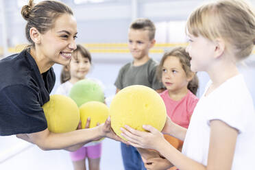 Glücklicher Lehrer, der einem Schüler auf dem Schulsportplatz einen Ball gibt - WESTF25153