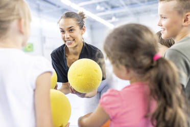 Lehrer im Gespräch mit Schülern, die auf dem Schulsportplatz einen Ball halten - WESTF25154