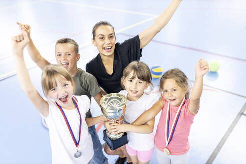 Lehrer feiert Sieg mit Schülern, die den Pokal auf dem Schulsportplatz halten - WESTF25155