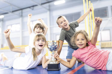 Students cheering with each other holding trophy at school sports court - WESTF25163