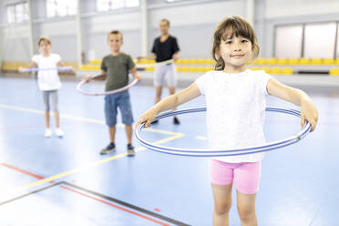 Lächelndes Mädchen mit Hula-Hoop-Reifen auf dem Schulsportplatz - WESTF25171