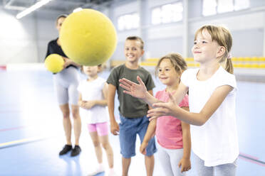 Lächelndes Mädchen fängt Ball mit Freunden auf dem Schulsportplatz - WESTF25174