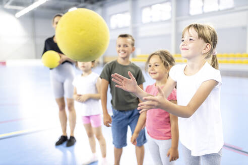 Lächelndes Mädchen fängt Ball mit Freunden auf dem Schulsportplatz - WESTF25174