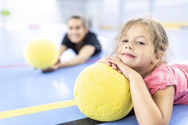 Mädchen ruht sich auf einem gelben Ball aus, der auf dem Schulsportplatz liegt - WESTF25180