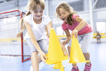 Playful girls picking up cones at school sports court - WESTF25187