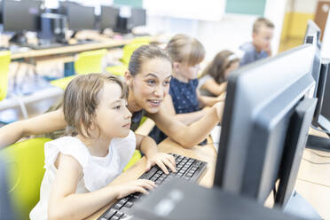 Student using computer with teacher in class at school - WESTF25196