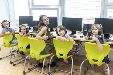 Lehrer und Schüler, die Daumen nach oben zeigen, sitzen auf einem Stuhl im Computerkurs in der Schule - WESTF25206