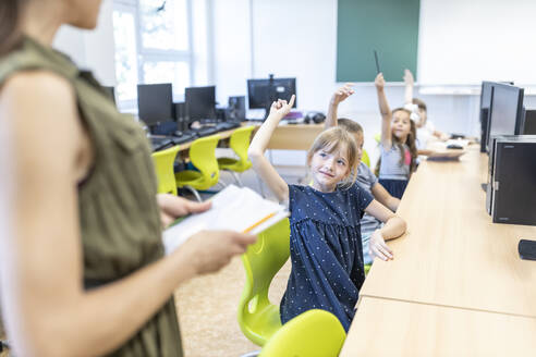 Schüler mit erhobener Hand, die den in der Klasse stehenden Lehrer anschaut - WESTF25217