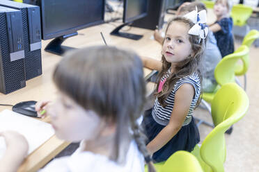 Mädchen sitzt am Schreibtisch mit Freunden im Klassenzimmer in der Schule - WESTF25223