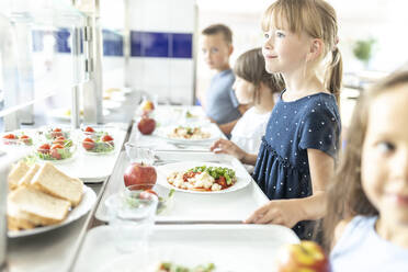 Girl with blond hair holding lunch tray at school cafeteria - WESTF25236