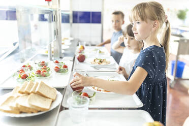 Mädchen nimmt Apfel beim Mittagessen in der Schulcafeteria - WESTF25237