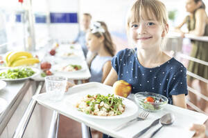 Lächelndes Mädchen hält Essenstablett in der Schulcafeteria - WESTF25240