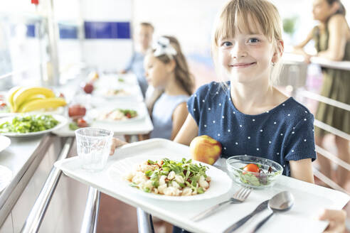 Smiling girl holding food tray in school cafeteria - WESTF25240