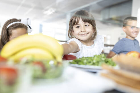 Lächelndes Mädchen nimmt Banane in der Mittagspause in der Schulcafeteria - WESTF25246