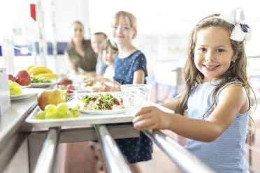 Lächelnde Schülerin mit Obst und Essen auf dem Tablett in der Mittagspause - WESTF25250