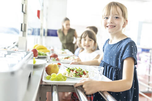 Blonde lächelnde Schülerin mit gesundem Essen in der Schulcafeteria - WESTF25251