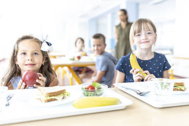 Mädchen mit Apfel und Banane am Tisch in der Cafeteria - WESTF25255