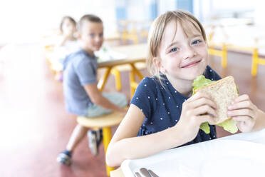 Smiling student holding sandwich at lunch break in cafeteria - WESTF25262