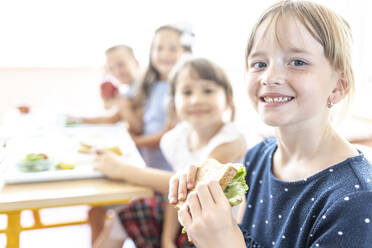 Student holding fresh sandwich with friends in background at cafeteria - WESTF25263