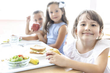 Smiling elementary student with food tray on table at lunch break in cafeteria - WESTF25265