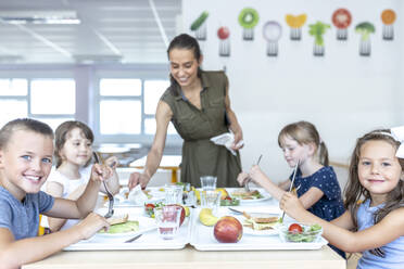 Lächelnde Schüler beim gemeinsamen Mittagessen mit einem Lehrer in der Cafeteria - WESTF25267