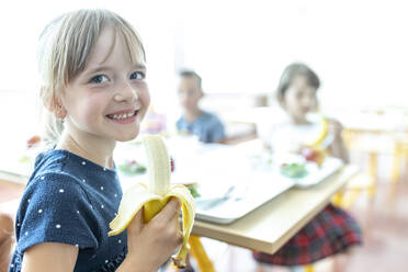 Lächelndes Mädchen mit Banane in der Mittagspause in der Cafeteria - WESTF25268