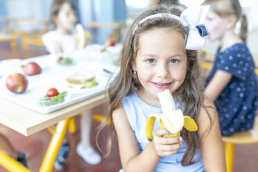 Mädchen mit Stirnband und Banane in der Mittagspause in der Cafeteria - WESTF25269