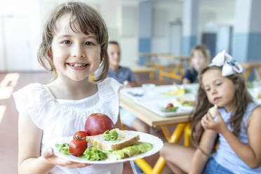 Lächelnder Schüler mit gesundem Essen auf einem Teller in der Cafeteria - WESTF25272