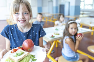 Mädchen hält Teller mit Apfel und Sandwich in der Mittagspause in der Schulcafeteria - WESTF25274