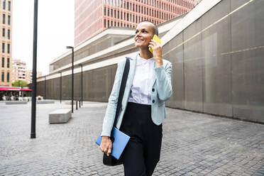 Lächelnde Geschäftsfrau, die am Fußweg mit einem Smartphone spricht - OIPF02514