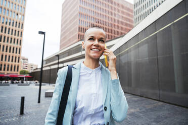 Glückliche Geschäftsfrau, die am Fußweg mit ihrem Smartphone spricht - OIPF02515