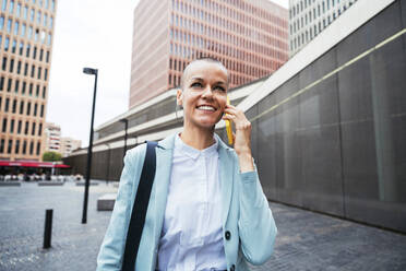 Happy businesswoman talking on smart phone at footpath - OIPF02515