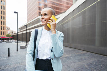 Lächelnde Geschäftsfrau, die vor einem Gebäude mit einem Smartphone telefoniert - OIPF02516