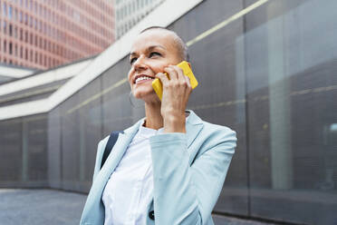 Lächelnde Geschäftsfrau, die auf dem Gehweg mit einem Mobiltelefon spricht - OIPF02517