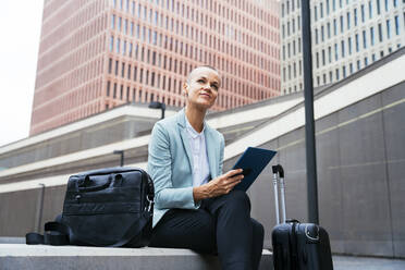 Contemplative businesswoman sitting with tablet PC in front of building - OIPF02524