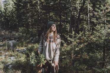 Contemplative woman with basket of spruce twigs in forest - VBUF00193