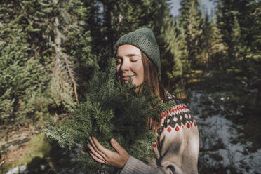 Woman with eyes closed holding twigs of spruce tree - VBUF00196
