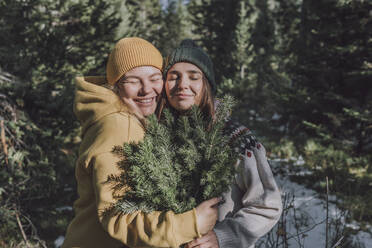 Lächelnde Freunde mit Fichtenzweigen, die sich im Wald umarmen - VBUF00199